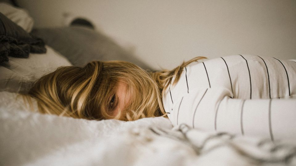 Kvinne ligger og hviler i sengen, tydelig sliten